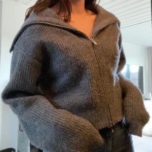 Stickad tröja - Säljer en mysig grå stickad kofta med dragkedja och bred krage. Koftan har en avslappnad passform och långa ärmar. Något nopprig