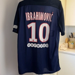 PSG fotbollströja med Ibrahimović 10 - Säljer en äkta PSG fotbollströja från Nike med Ibrahimovićs namn och nummer 10 på ryggen. Tröjan är mörkblå med en röd och vit rand i mitten. Den har korta ärmar och är tillverkad i Dri-FIT material för optimal komfort.