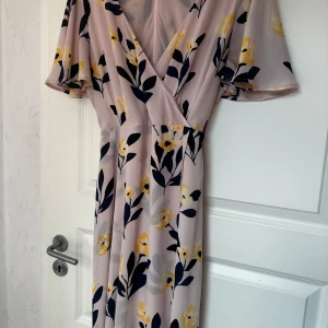 Blommig omlottklänning från Stockh LM - Säljer en ljus, blommig omlottklänning från Stockh LM i storlek 42. Klänningen har korta ärmar, v-ringning och knytband i midjan. Mönstret består av gula och mörkblå blommor på en ljus botten. Perfekt för sommarens tillfällen! Passar till de som har 40 storlek också 