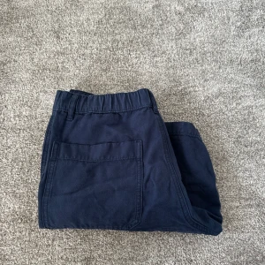 Mörkblå shorts med fickor - Säljer ett par mörkblå shorts med klassisk passform. Shortsen har två sidofickor och bakfickor, samt hällor för bälte och stängs med knapp och dragkedja. Shjortens är i bra skick och har använts sparsamt. Märke uniqlo. Nypris 349 mitt pris 149.