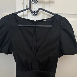 Svart klänning från Bik Bok - Snygg svart klänning från Bik Bok i storlek XS. Den har en v-ringad design med korta ärmar och en dragkedja i ryggen. Perfekt för en stilren look.