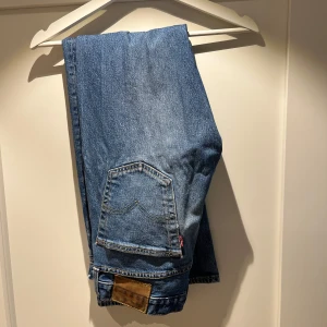 Levis 501:or nypris 1200 kr - Säljer ett par klassiska blå jeans från Levi's med en rak passform. De har en traditionell femficksdesign och en knappgylf. Perfekta för en avslappnad stil.