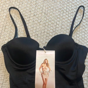 Svart shaping-korsett från Victoria's Secret - Säljer en svart shaping-korsett från Victoria's Secret med justerbara axelband och vadderade kupor. Sitter tight och formar kroppen snyggt. Perfekt under klänningar eller toppar för en slät siluett. Säljer då den är för liten. Helt ny med lapp!