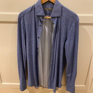 Blå skjorta från Corneliani - Säljer en klassisk blå skjorta från Corneliani. Skjortan har knappar framtill och en stilren krage. Perfekt för dig som gillar en tidlös och snygg look. Passar till många olika tillfällen. Aldrig använd, mint skick! Storlek M