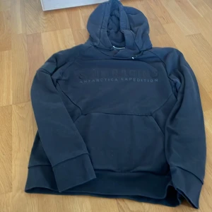 Sailracing hoodie svart stl XS herr - Svart hoodie från Sail Racing med trycket 'SAIL RACING ANTARCTICA EXPEDITION' på bröstet. Tröjan har huva med dragsko och en stor magficka. Herr storlek XS. 