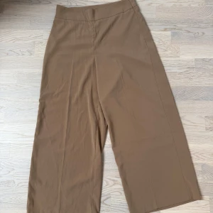 Beiga vida kostymbyxor - Snygga beiga kostymbyxor med vida ben och hög midja. Byxorna har en stilren design utan synliga detaljer och är perfekta för en dressad look. Tillverkade i ett mjukt och följsamt material som ger en skön känsla.