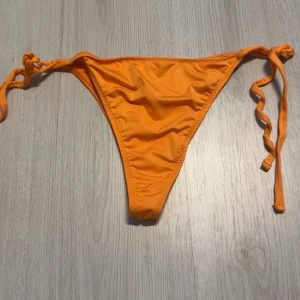 Orange bikiniunderdel med knyt - Snygg orange bikiniunderdel med knyt i sidorna. Perfekt för soliga dagar på stranden eller vid poolen. Den har en enkel och stilren design som ger en fräsch look.
