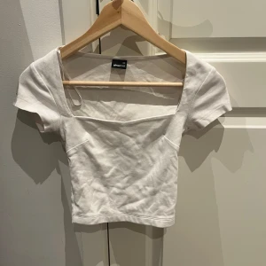 Vit kortärmad topp från Gina Tricot - Säljer en stilren vit topp från Gina Tricot i storlek XS. Toppen har korta ärmar och en elegant fyrkantig urringning. Perfekt för en minimalistisk look. Säljer pga den är för liten, bara använd fåtal gånger