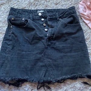 Svart jeanskjol med knappar - Svart jeanskjol från Gina Tricot med knappar framtill och rå kant nedtill. Kjolen har en omlott-design och praktiska fickor både fram och bak. 💖