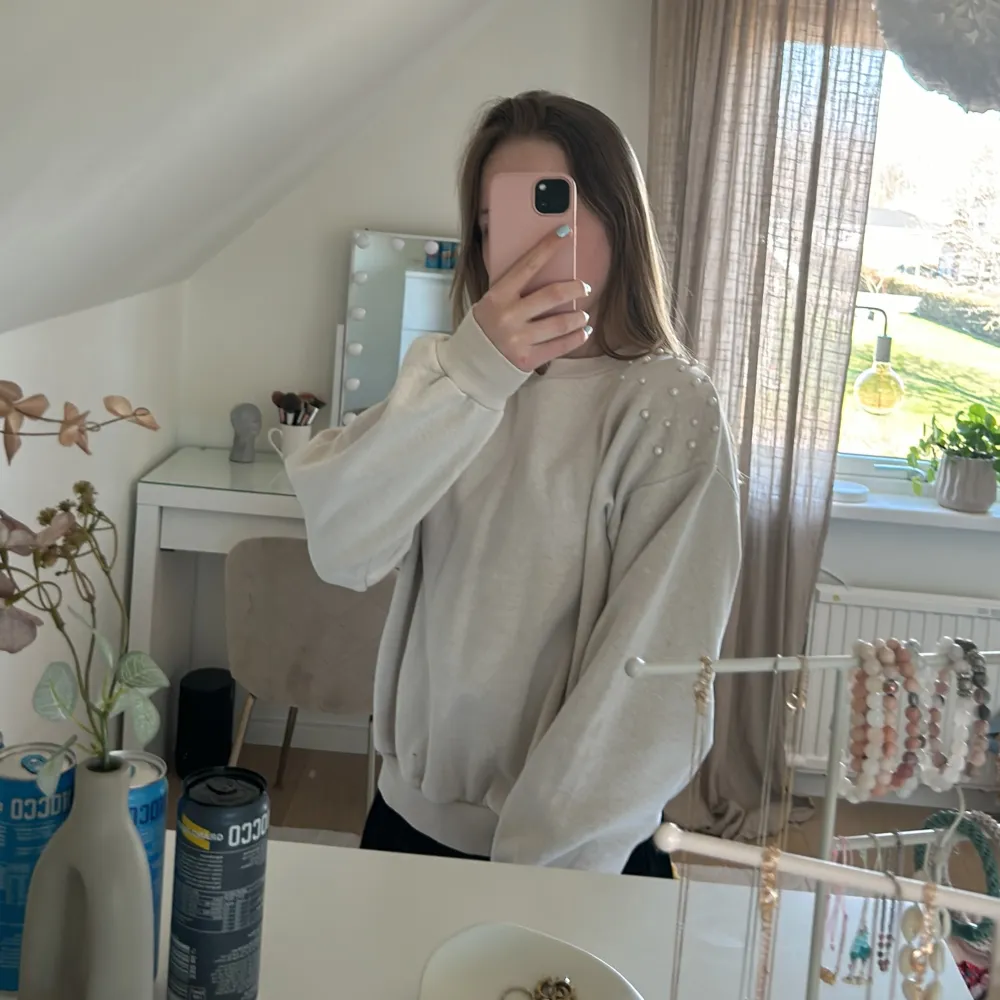 Säljer en stilren beige tröja med pärldetaljer på axlarna. Tröjan har långa ärmar och en bekväm passform, perfekt för en avslappnad look. Den är gjord i ett mjukt material som känns skönt mot huden.. Neuletakit & Villapaidat.