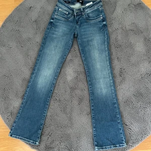 Blå bootcut jeans från LTB W24 L30 - Snygga blå jeans från LTB med bootcut passform och låg midja. Jeansen har klassisk femficksdesign, dragkedja och knapp framtill samt diskreta slitningar för en cool look. Tillverkade i mjukt denim-material som sitter skönt hela dagen.