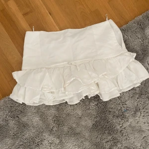 Vit volangkjol från Zara - Supersöt vit kortkjol från Zara med dubbla volanger och en lätt A-linjeform. Kjolen är gjord i ett mjukt bomullstyg som känns luftigt och fräscht. Perfekt för dig som gillar romantiska detaljer och vill ha en kjol som sticker ut med sin volangkant. Passar även S 
