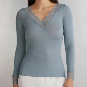 Ljusblå långärmad topp med spets - Supersnygg ljusblå långärmad topp med v-ringning och spetsdetaljer både vid halsringningen och ärmsluten. Toppens material är tunt och stretchigt, vilket ger en slim passform och en fräsch look.