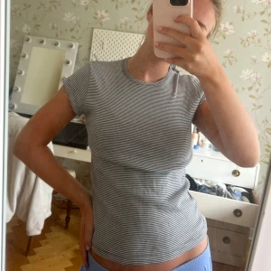 Randig t-shirt från Brandy Melville - Superenkel och snygg t-shirt från Brandy Melville med smala svarta och vita ränder. Modellen är figurnära med korta ärmar och rund halsringning. Perfekt till jeans eller kjol för en chill och stilren look.