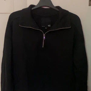 Svart half zip sweatshirt från 157 - Svart sweatshirt från 157 med halv dragkedja och hög krage. Tröjan har lång ärm och en clean, enkel look som funkar till jeans eller mjukis. Materialet känns mjukt och är troligtvis bomull eller polyester. Perfekt för chill dagar eller när du vill vara bekväm.