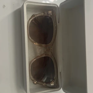 Beige CHIMI solglasögon med fodral modell 07 - Snygga solglasögon från CHIMI med transparent beige båge och stora, fyrkantiga glas. Kommer med originalvitt hårt fodral och tygpåse. Perfekta för att lyfta din stil med en modern touch. 