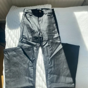 Svarta skinn byxor från ONLY - Snygga svarta skinn byxor från ONLY med fem fickor och utsvängda ben. Byxorna har en glansig finish som ger en cool look och är perfekta för dig som vill sticka ut. Klassisk knapp och dragkedja framtill samt bälteshällor i midjan.