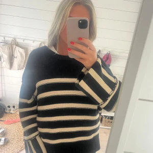 Dagmar tröja - Säljer en oversized stickad tröja med breda svarta och vita ränder. Tröjan har långa, vida ärmar och en klassisk rund halsringning. Perfekt för dig som gillar en chill och trendig look med lite extra volym i ärmarna. Storlek L men passar M