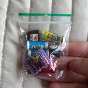 Söta godisberlocker till smycken - Samling med 8 färgglada berlocker som ser ut som godisförpackningar: Nutella, Maltesers, Pringles, Haribo och Sour Pickle. Perfekta att använda till armband, halsband eller örhängen. Mix av röd, blå, gul, lila och svart, med roliga detaljer och metallöglor för enkel montering.