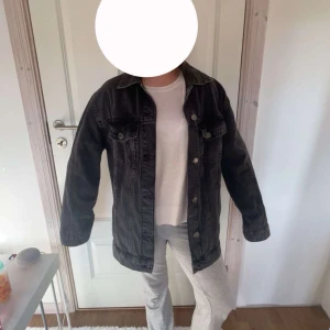 Svart jeansjacka från Kappahl XS - Säljer en svart jeansjacka från Kappahl i storlek XS. Jackan har klassisk krage, knäppning framtill med silverfärgade knappar och två bröstfickor med lock. Modellen är rak och lite oversized, perfekt till lager-på-lager-stil. Den är oanvänd & det följer med en extra knapp. Pris kan diskuteras 