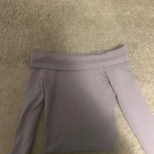Ljuslila offshoulder topp  - Supersnygg ljuslila, croppad offshoulder topp från Clockhouse i storlek XS. Toppen har långa ärmar och en bred kant upptill som ger en clean och trendig look. Perfekt att styla med jeans eller kjol för en cool vibe.