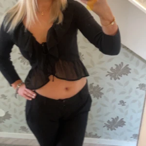 Svart volangblus från Amisu - Supersöt svart blus från Amisu med volangkant längs den djupa v-ringningen och nertill. Toppen är croppad och har lång ärm samt knyt 🌸 Pris kan diskuteras såklart