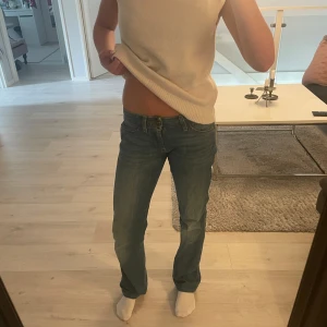 Wrangler blå bootcut jeans - Snygga blå jeans från Wrangler med klassisk bootcut-passform och låg midja. Jeansen är tillverkade i bomull med lite stretch för extra komfort. De har fem fickor, bälteshällor och en cool tvättad look. Perfekta för dig som gillar en avslappnad men stilren vibe.