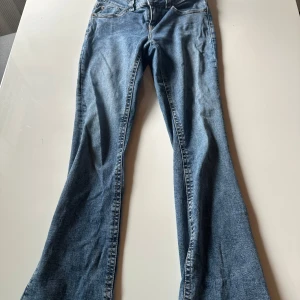 Blå bootcut jeans från Perfect Jeans - Snygga blå bootcut jeans från Perfect Jeans i klassisk denim. Byxorna har två bakfickor med lock och knapp, samt normal midja. Perfekt för dig som gillar en retroinspirerad look med utsvängda ben.