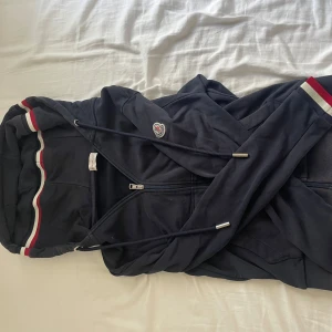 Mörkblå moncler hoodie. - Mörkblå ziphoodie från moncler med snörning.. Ärmar och huva har snygga rödvita ränder. Hoodien har Moncler-logga på armen och praktiska fickor. Storlek S/M. Pris går att diskutera, och ställ gärna frågor.