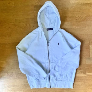 Ralph Lauren Zipup - Tröjan är i mycket bra skick och är gjord i ett skönt och bra material. Den har storleken L, fast passar även M. Den har en svag fläck precis under loggan som går att se i bild 2.                Kontakta mig och du har några frågor eller om du vill ha fler bilder.