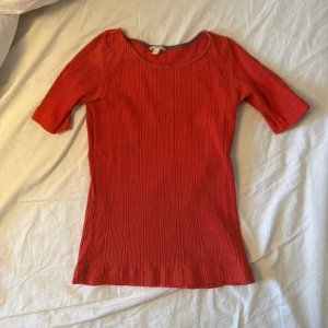 Röd ribbad topp  - Säljer en röd ribbad topp med rund halsringning och halvlånga ärmar. Toppen har en slim passform och är tillverkad i mjuk bomull, perfekt för en enkel men snygg look.