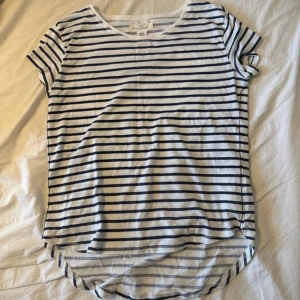 Randig vit t-shirt från H&M - Vit t-shirt med svarta horisontella ränder från H&M. Modellen har rund hals och korta ärmar, samt en något längre och rundad nederkant bak. Perfekt för en chill och enkel stil. Materialet är mjuk bomull som känns skönt mot huden.