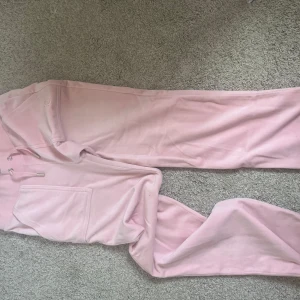 Ljusrosa mjukisbyxor från Juicy Couture - Jag säljer mina super fina ljusrosa mjukisbyxor från Juicy Couture i storlek xs. De har bred resår i midjan och snörning med silverdetaljer. Jätte mysigt material och har ingen synlig användning(använda fåtal gånger) då de är för stora för mig. Hör av er för mer info eller bilder! Köpta för 1200