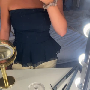 Mörkblå bandeau tubtopp med volang - Snygg mörkblå bandeau tubtopp från Cubus i storlek S. Toppen är axelbandslös och har en volangkant nedtill som ger en extra touch. Materialet är lätt och har ett skirt lager som gör toppen luftig.