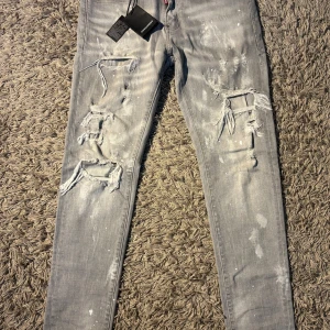Gråa Dsquared2 jeans - Riktigt snygga grå jeans från Dsquared2 med slitna detaljer och stora hål framtill. Jeansen har skinny passform, coola färgstänk och klassisk femficksdesign. Perfekta för dig som gillar streetstyle och vill sticka ut lite extra.