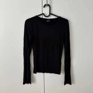 Svart långärmad topp från Gina Tricot - Svart långärmad topp från Gina Tricot i mjuk bomull. Modellen är slim och har rund halsringning. Ärmarna har en cool slitsdetalj längst ner som ger en extra edge till looken. Perfekt att styla med jeans eller kjol för en clean vibe. Som ny 😍