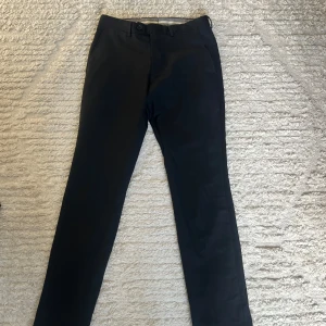 Svarta kostymbyxor These Glory Days - Snygga svarta kostymbyxor från These Glory Days i slim fit-modell. Byxorna har raka ben, bälteshällor och knäppning fram. Perfekta för en clean och stilren look. Skandinavisk design med klassiska detaljer. Passar bra om du är 170.