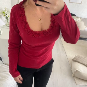 Röd långärmad topp med volang - Säljer en snygg röd långärmad topp med volangdetaljer runt den fyrkantiga ringningen. 