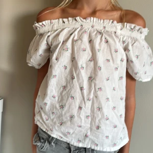 Offshoulder blommig topp H&M - Supersöt offshoulder topp från H&M i vit bomull med små rosa blommor och gröna blad. Puffiga korta ärmar och smock upptill som ger en romantisk vibe. Perfekt för varma dagar och ger en riktigt somrig känsla.