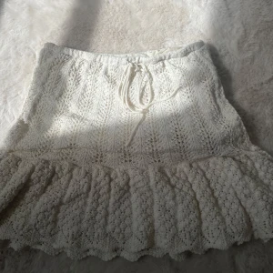 Vit stickad kjol  - Nästan aldrig använd.Supersöt vit stickad kjol från Zara med volangkant och snygg snörning i midjan. Kjolen har ett detaljerat mönster och är perfekt för dig som gillar en romantisk och boho-inspirerad stil. Passar dig som vill ha en ljus och fräsch look.