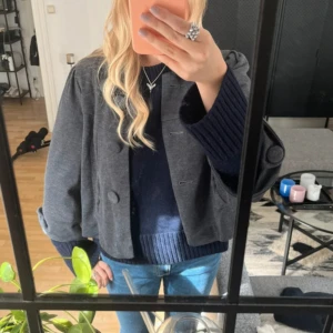 Grå trekvartsärmad jacka  - Säljer en grå trekvartsärmad jacka / kappa med stora, klädda knappar framtill. Jackan har trekvarts ärm, vilket ger en trendig look. Perfekt att slänga över en stickad tröja och jeans för en cool vardagsstil. Aldrig använd, köpte på plick 