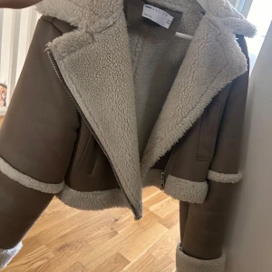 Beige teddyjacka från ASOS Design - Säljer en beige teddyjacka från ASOS Design med krage och detaljer i mjuk, vit teddyfleece. Jackan har dragkedja framtill, fickor och uppvikta ärmslut. Perfekt för dig som vill ha en snygg och mysig look under höst och vinter.