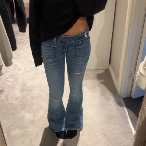 Blå bootcut jeans Gina Tricot XXS - Snygga blå bootcut jeans från Gina Tricot 14+ i storlek XXS. Jeansen har låg midja, slitna detaljer vid knäna och stora fickor framtill. Tillverkade i  denimtyg med en utsvängd passform. Helt oanvända.