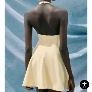 Ljusgul kort klänning med halterneck - Supersöt ljusgul klänning med halterneck och öppen rygg. Modellen är kort med utsvängd kjol och har en clean, modern look. Perfekt för sommarens alla tillfällen. Klänningen stängs med dragkedja bak och har en figurnära passform upptill. I stl s och bara använd en gång💕