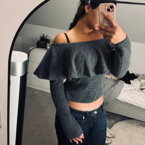 Grå offshoulder stickad tröja H&M - Superfin grå stickad tröja från H&M med offshoulder och bred volang över axlarna. Croppad modell som sitter snyggt och har långa ärmar. Perfekt för dig som gillar trendiga detaljer och vill ha en mysig men stilren look.