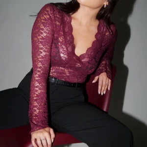 Vinröd spetsblus med v-ringning - Vinröd långärmad blus i transparent spets från Gina Tricot. Toppen har en djup v-ringning med vågig kant och är figurnära. Perfekt för dig som vill sticka ut med en romantisk och trendig look.