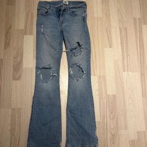Blå bootcut jeans med slitningar XS - Snygga blå bootcut jeans från 157 i storlek XS. Jeansen har coola slitningar och hål på båda benen framtill för en trendig look. Klassisk femficksmodell och full längd. Perfekta för dig som gillar en avslappnad och edgy stil.