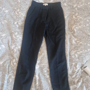 Svarta kostymbyxor med raka ben - Snygga svarta kostymbyxor med raka ben och klassisk passform. Byxorna har fickor fram och passpoalfickor bak samt hällor för bälte. Perfekta för en clean och stilren look.