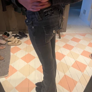 gråa True Religion bootcut jeans - Säljer ett par gråa  jeans från True Religion med bootcut passform. Jeansen har snygga detaljer som stora fickor med lock och silverfärgade knappar bak. Klassisk femficksmodell och låg midja. Materialet är stretchigt jeans för en bekväm känsla. säljer pg för små!