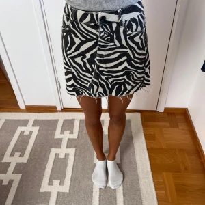 Zebramönstrad jeanskjol  - Cool kort jeanskjol med svartvitt zebramönster och rå, fransig kant nertill. Klassisk femficksmodell med bälteshällor och dragkedja fram. Perfekt statement-plagg för dig som vill sticka ut.